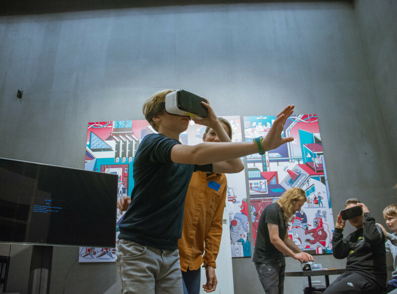 E! Ein Workshopteilnehmer trägt eine VR-Brille und greift nach einem für uns nicht sichtbarem Gegenstand im virtuellen Raum.