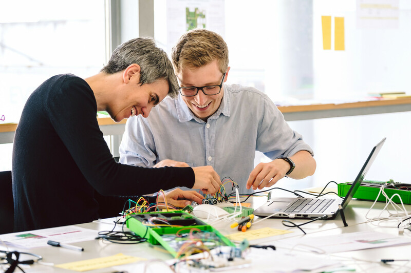 E! Zwei Workshopteilnehmer stecken Kabel in einen Mikrocontroller.