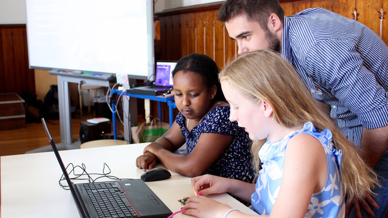 Zwei Schülerinnen zeigen einem Trainee, was sie mit Calliope mini programmiert haben.