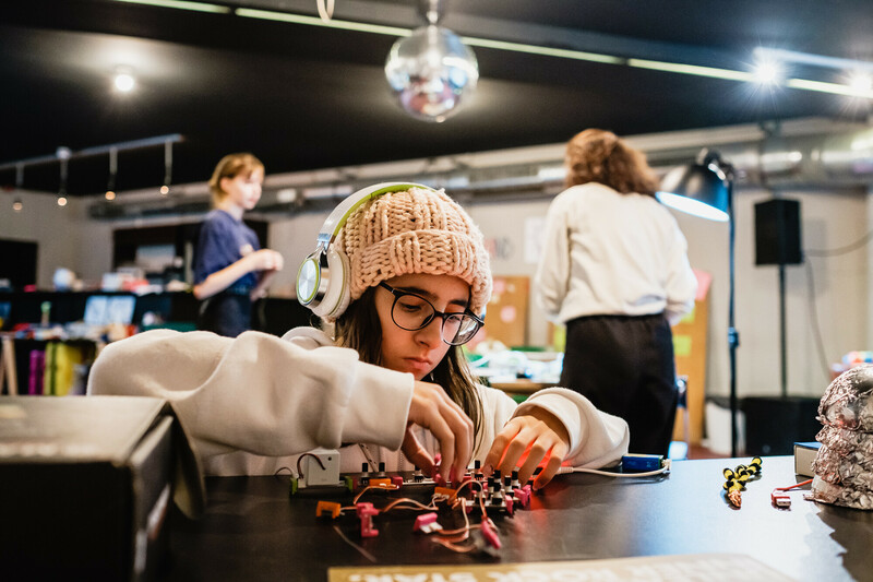 E: Ein Mädchen werkelt an einem Prototyp, verbindet elektronische Elemente mit Kroko-Klemmen und Kabeln.