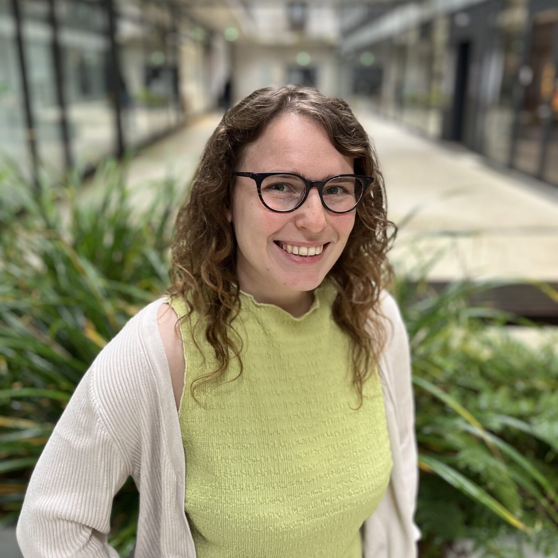 Zeigt eine lächelnde Frau vor einem Hintergrund mit Pflanzen